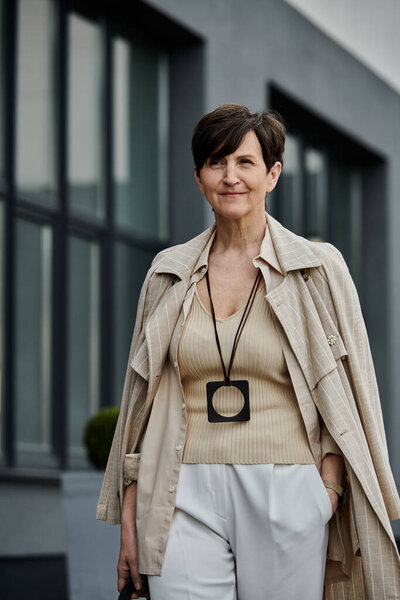 A fashionable woman walks confidently down a city street carrying a stylish handbag.