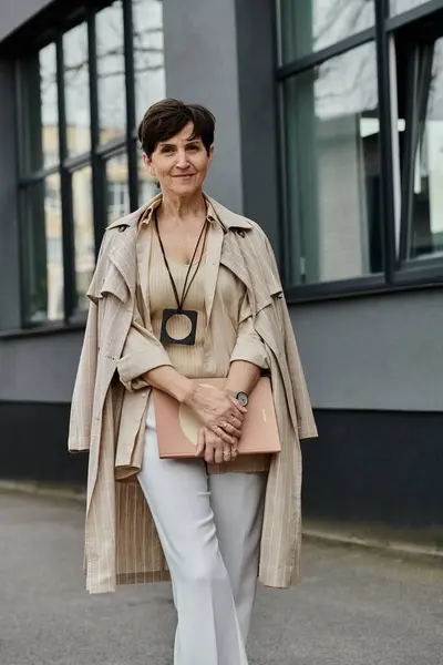 stock image A woman in a tan coat and white pants walking with purpose.