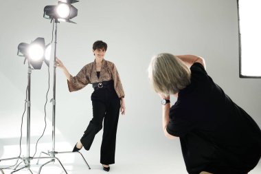 Orta yaşlı bir kadın, elinde fotoğraf makinesi olan bir fotoğrafçıyla ışık patlamasında poz veriyor ve fotoğraf sanatını sergiliyor..