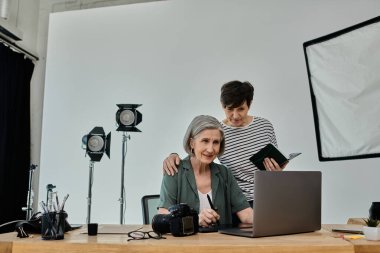 Çift, profesyonel bir fotoğraf stüdyosunda dizüstü bilgisayarda çalışırken yan yana oturur..