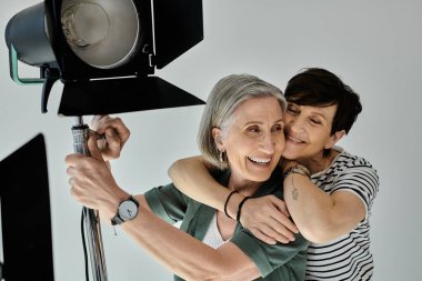 Softbox 'ın önünde profesyonel bir fotoğraf stüdyosunda sarılan orta yaşlı lezbiyen çift.