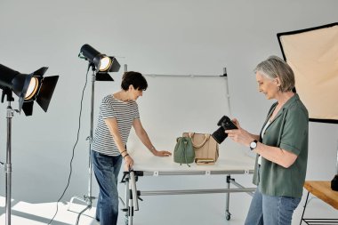 Orta yaşlı bir çift, biri kamera tutuyor, modern bir fotoğraf stüdyosunda iş birliği yapıyorlar..