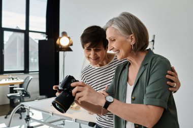 Modern bir stüdyoda tutkulu bir şekilde fotoğraf makinesi tutan orta yaşlı bir lezbiyen çift.