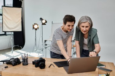 İki orta yaşlı kadın, profesyonel bir fotoğraf stüdyosunda dizüstü bilgisayarda birlikte çalışıyorlar..