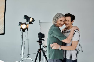 Orta yaşlı bir lezbiyen çift profesyonel bir fotoğraf stüdyosunda kameranın önünde sarılıyor..