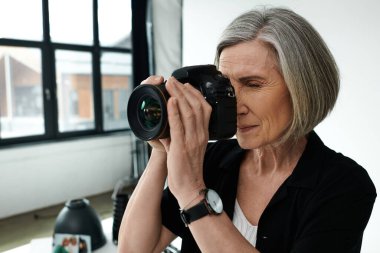 Orta yaşlı bir kadın fotoğraf stüdyosunda fotoğraf çekiyor. Elinde kamera var. Yaratıcılık sergiliyor..