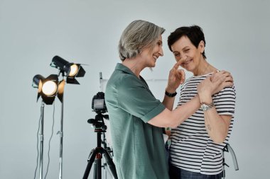İki kadın, orta yaşlı lezbiyen çift, profesyonel bir fotoğraf stüdyosunda kameranın önünde güvenle dururlar..