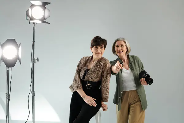 stock image A middle-aged lesbian couple in a photo studio, one capturing with a camera, the other posing as a model.