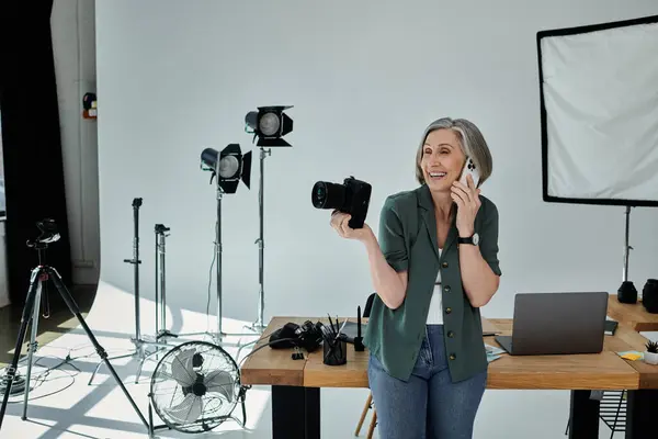 stock image happy woman multitasking, holding a camera and chatting on a cell phone.