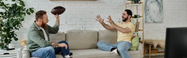 Two bearded men and their labrador dog sit on top of a couch, watching a sports match in their cozy living room. clipart