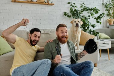 Labrador köpeği olan bir çift adam oturma odasında maç izlerken tezahürat yapıyor..