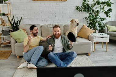 İki sakallı adam, kanepede Labrador 'larıyla oturup televizyonda beyzbol maçı izlemenin keyfini çıkarıyorlar..