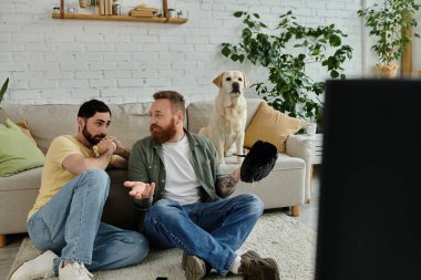 Labrador köpekli iki adam, sıcak bir oturma odasında kanepede oturmuş beyzbol maçı izliyorlar..