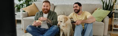 Sakallı iki adam bir labrador ile kanepede oturuyor, sıcak bir oturma odasında komedi filminin keyfini çıkarıyorlar..