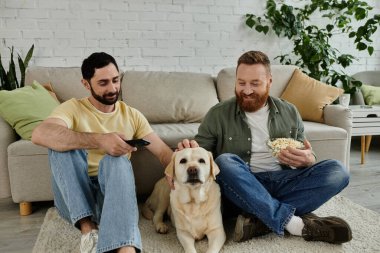 İki sakallı adam kanepede oturup patlamış mısır yerken Labrador köpeği de sıcak bir oturma odasında oturmuş....