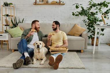 İki adam, sakallı eşcinsel bir çift, bir kanepede oturup pizza yerken Labrador köpeği yakınlardaki bir oturma odasında oturmuş,.