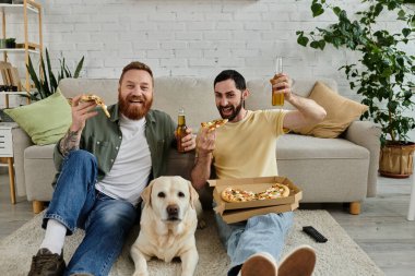 Two men with beards enjoy pizza and beer on a couch with their Labrador dog in a cozy living room setting. clipart