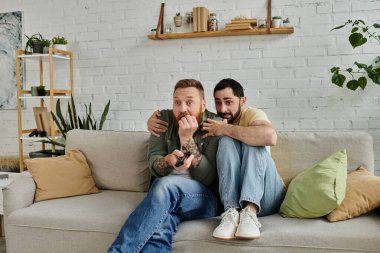 Kanepede oturan iki sakallı adam, kollarını birbirlerine dolamış, oturma odalarında şefkat ve yakınlık gösteriyorlar..