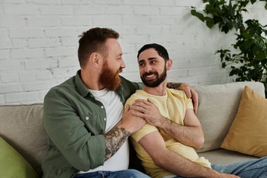 Bir çift sakallı adam rahatlar ve rahat bir oturma odasında koltuğun üstünde sohbet ederler..