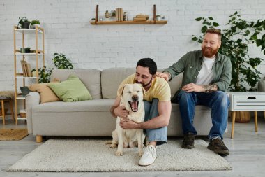 Sakallı iki adam kanepede oturmuş, keyifli Labrador köpekleriyle hoş vakit geçiriyorlar..