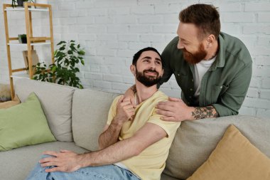 Modern bir kanepede uzanan sakallı eşcinsel bir çift, oturma odasında Labrador 'larıyla samimi bir anı paylaşıyorlar..