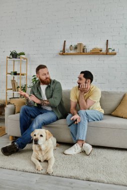 İki adam, biri sakallı, kanepede dost canlısı bir Labrador ile oturma odasında oturuyor..