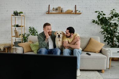 İki sakallı adam kanepede oturup, labradorlarıyla sıcacık bir oturma odasında sarılıyorlar..