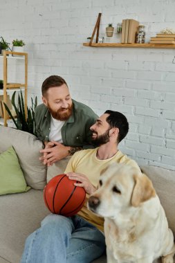 Sakallı adam, Labrador köpeğinin yanında, rahat oturma odasında basketbolla kanepede dinleniyor..