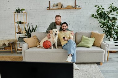 A bearded gay couple sitting comfortably on a couch, enjoying quality time with their loyal labrador in the living room. clipart