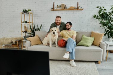 Two men with beards relax on a couch with their Labrador in a cozy living room setting. clipart