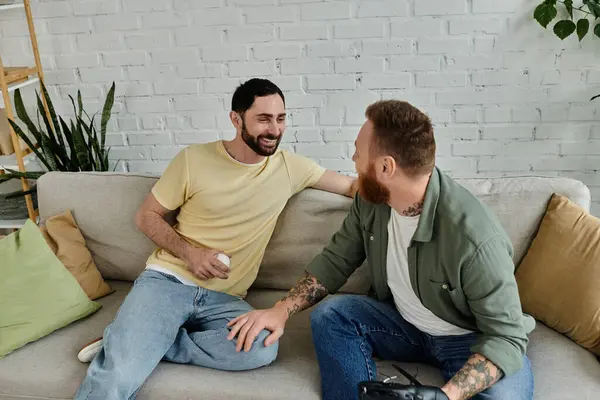 Stock image Bearded gay couple relax on couch, watching sports in cozy living room.