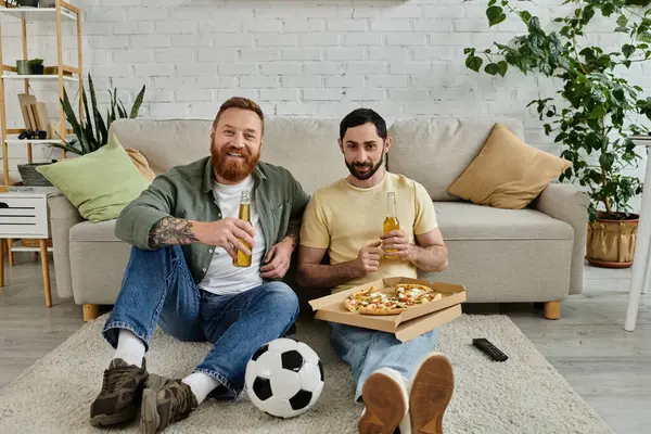 stock image Two men, a bearded gay couple, sit on the floor enjoying pizza and beer