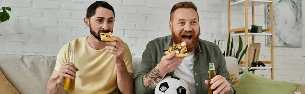 stock image Two men with beards relax on a couch, eating pizza, drinking beer