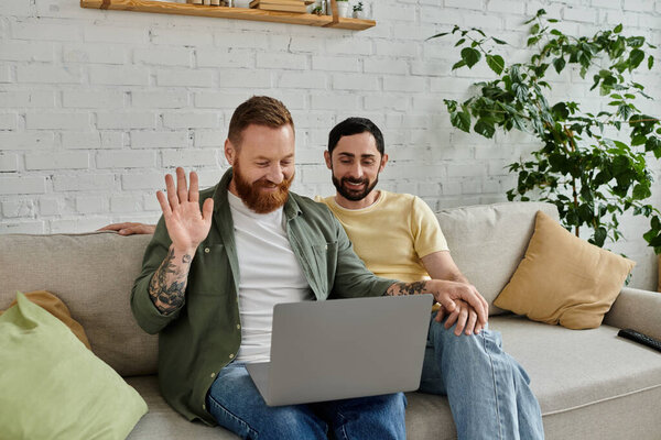 Бородатая гей-пара, сидящая на диване, сосредоточенная на экране ноутбука в уютной гостиной.