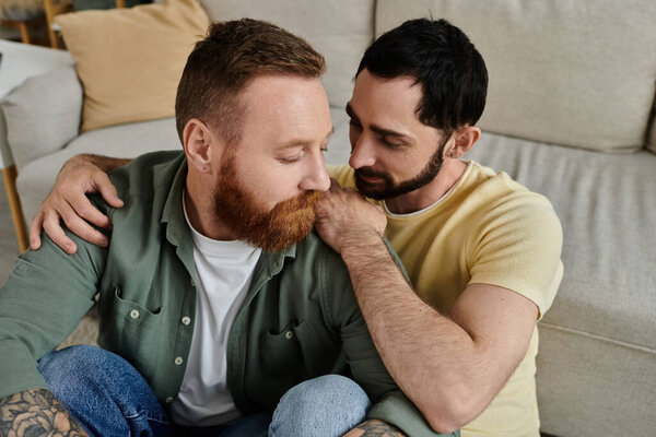 A cozy scene of a gay couple with beards, sitting closely together on the backrest of a couch in their living room.