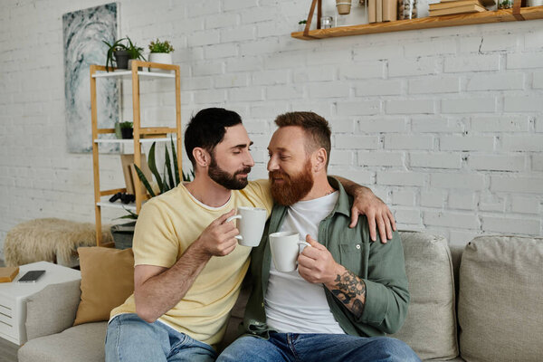 A bearded gay couple relaxes together, sitting on top of a couch in their living room, enjoying quality time.