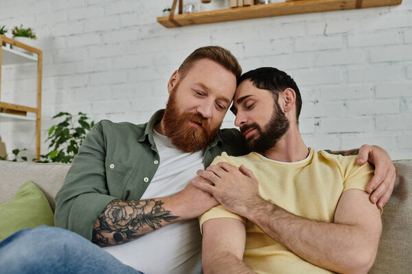 A couple of bearded men relax atop a couch, enjoying intimate moments together in their cozy living room.