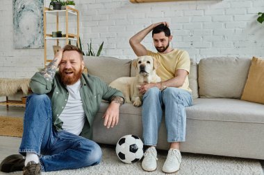 Oturma odasında, bir adam Labrador köpeğiyle bir kanepede oturur ve birlikte spor maçı izler..