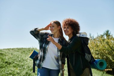 Two young women, one with curly hair and the other with straight hair, are hiking in the wilderness. clipart