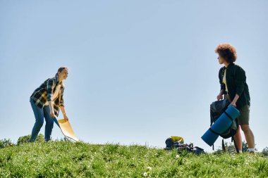 A young lesbian couple sets up camp in a grassy field on a bright sunny day. clipart