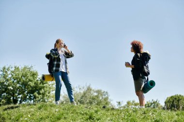 İki genç kadın, bir lezbiyen çift, vahşi doğada yürüyüş yapıyorlar, biri diğerinin fotoğrafını çekiyor..