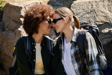 A young lesbian couple smiles at each other while hiking through the wilderness. clipart