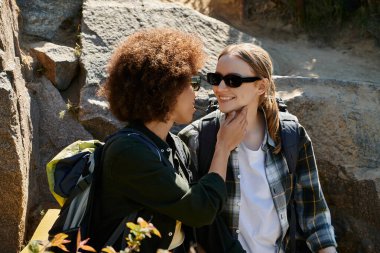 Biri kıvırcık saçlı, diğeri düz sarı saçlı genç lezbiyen bir çift yürüyüş sırasında mola verip vahşi doğanın ortasında hassas bir anı paylaşıyor..
