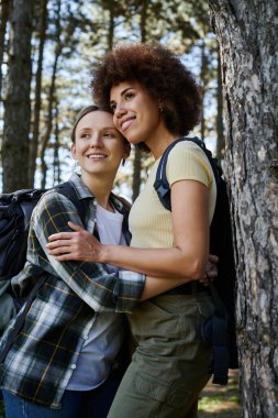 Genç bir lezbiyen çift, güneşli bir günde ormanda yürürken gülümser..