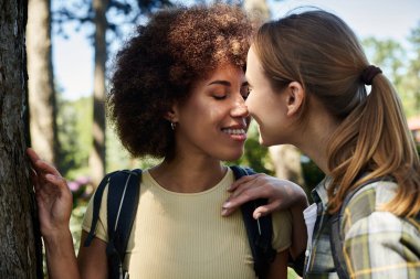 A young lesbian couple hikes through the woods, sharing a tender moment of connection. clipart