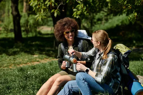 stock image Two young women, hike together in a green forest and share coffee.