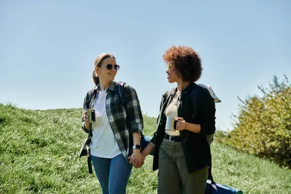 stock image Two young women, a lesbian couple, are hiking together on a sunny day. They are smiling and holding hands, enjoying their time in the wilderness.