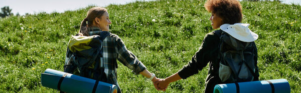 Two young women, hand in hand, hike through a grassy field.
