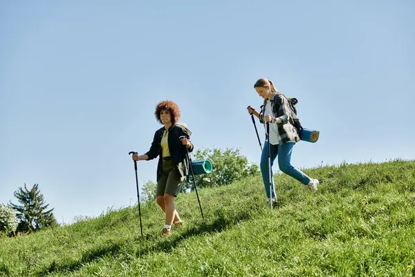 stock image Two young women, a lesbian couple, hike together through a beautiful green landscape, enjoying the outdoors.