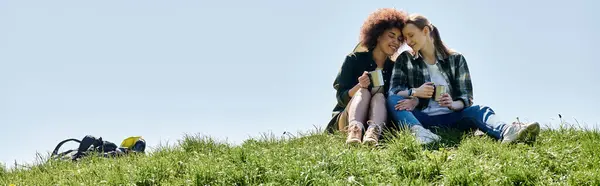 stock image A young lesbian couple enjoys a coffee break while hiking through a grassy field.